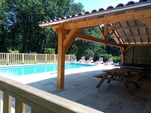 Ein überdachter Außenbereich mit Pool, Liegestühlen und einem Tisch.