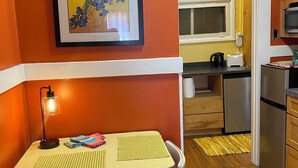 Cocina compacta con comedor, una obra de arte enmarcada en la pared y una pequeña mesa con sillas.