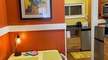 A compact kitchen with a dining area, a framed artwork on the wall, and a small table with chairs.