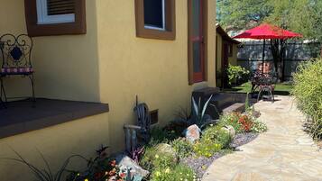 A yellow building with a stone pathway, a red umbrella, and various plants.
