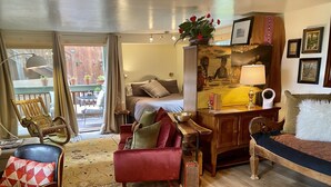 Habitació acollidora amb un llit, un escriptori, una cadira i un sofà. Hi ha una finestra amb cortines, una cadira de fusta i una catifa.
