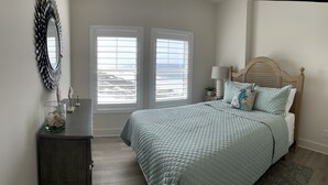 A bedroom with a bed, a dresser, a mirror, and a window with a view of the beach. - Sweeping Vue of the Gulf of Mexico, 30 steps to beach (Mexico Beach)
