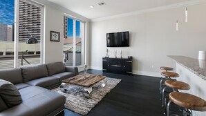 Una sala de estar moderna con un sofá gris, una mesa de centro de madera y una zona de bar con taburetes.