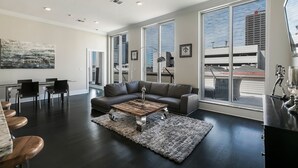 Una sala de estar moderna con piso de madera oscura, un sofá de cuero, una mesa de centro y ventanas amplias con vistas a la ciudad.