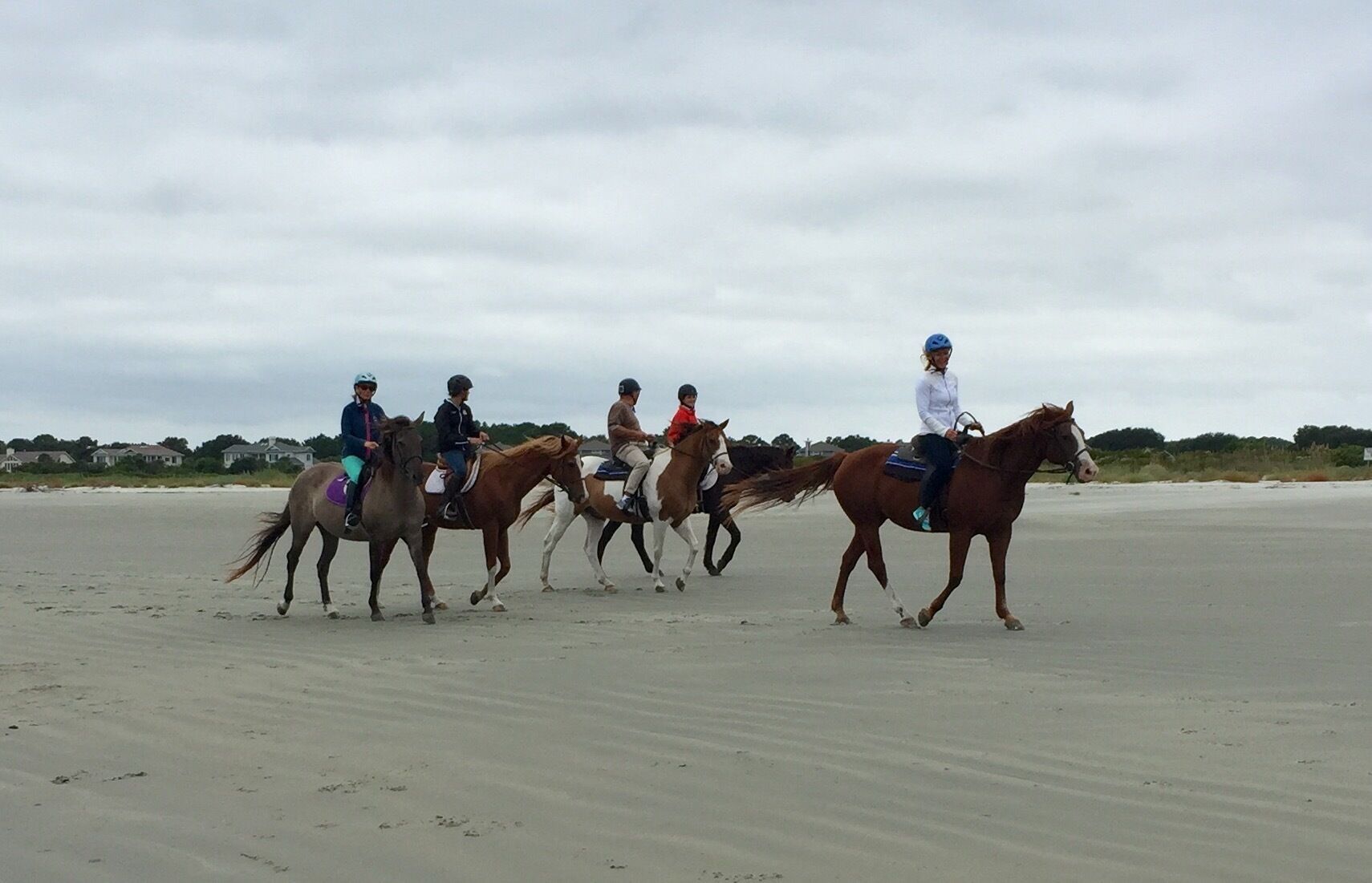 Un gruppo di persone cavalca cavalli su una spiaggia sabbiosa.