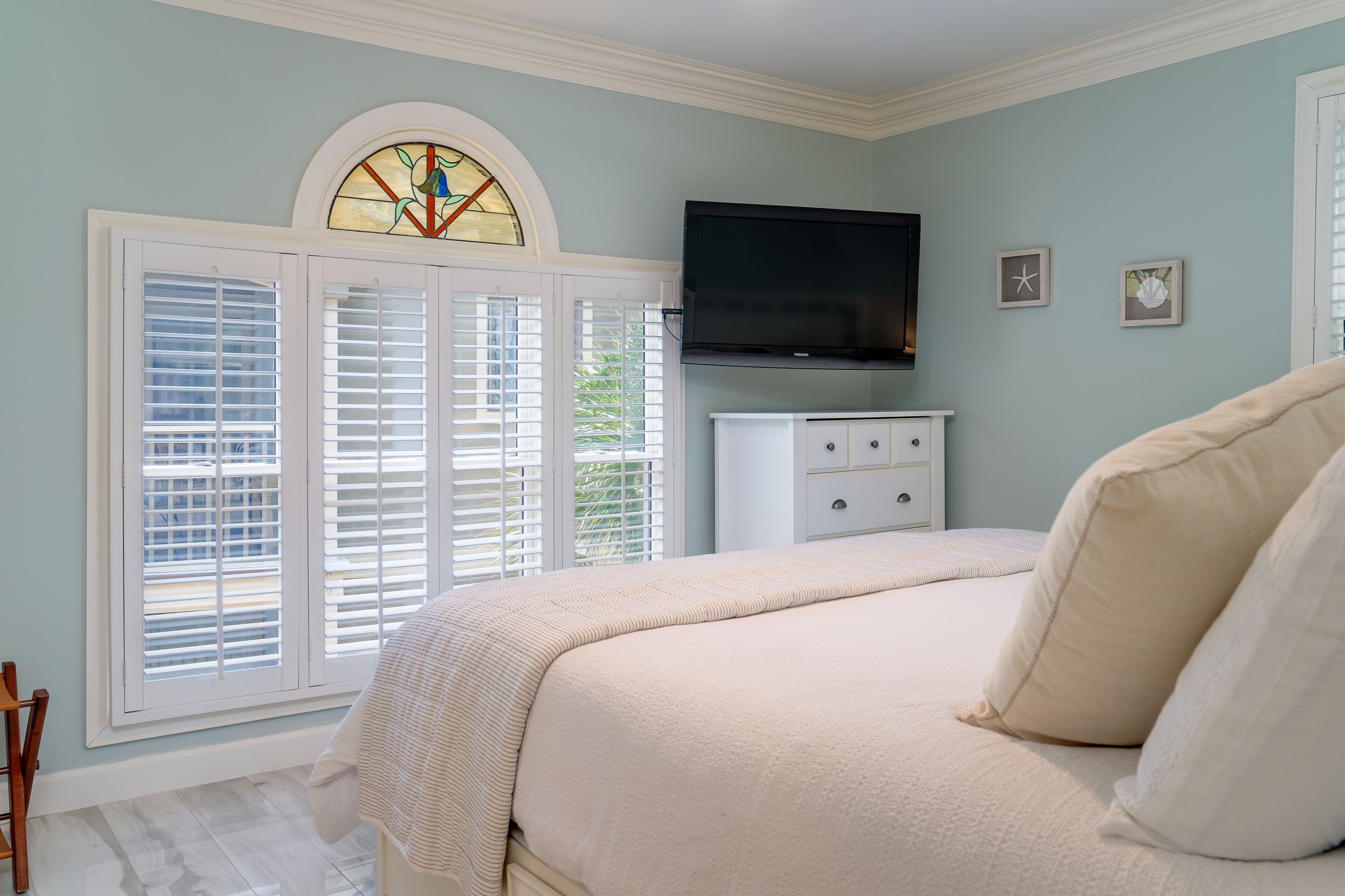 A bedroom with a bed, a television, a dresser, and a window with shutters.