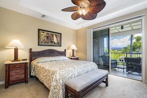 Une chambre dotée d’un grand lit, de deux tables de chevet avec des lampes, d’un ventilateur de plafond, d’une grande fenêtre donnant sur l’extérieur et d’un balcon avec des meubles de jardin.
