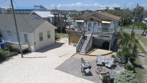 A beachfront property with a large house, a covered outdoor seating area, and a fire pit.