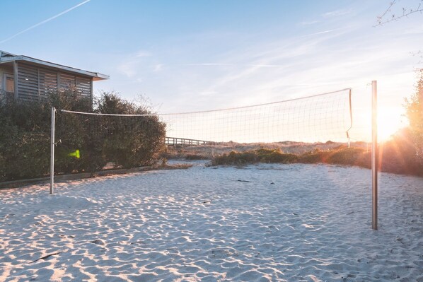 A beach volleyball court with a net, sand, and a building in the background.