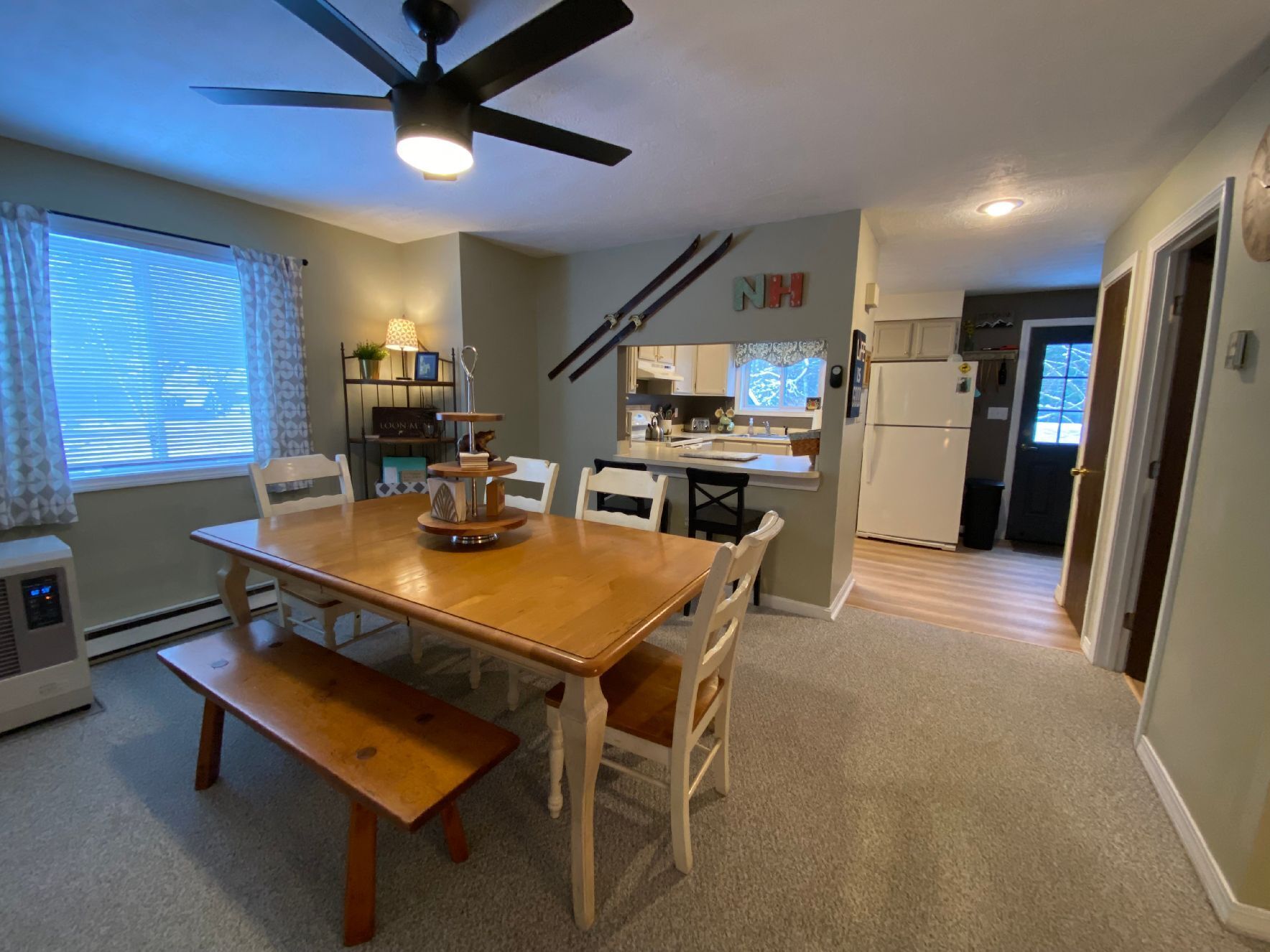 A dining area with a wooden table and chairs, a ceiling fan, and a kitchen in the background.