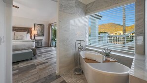 Un baño moderno con una bañera independiente, ducha y un amplio ventanal con persianas.