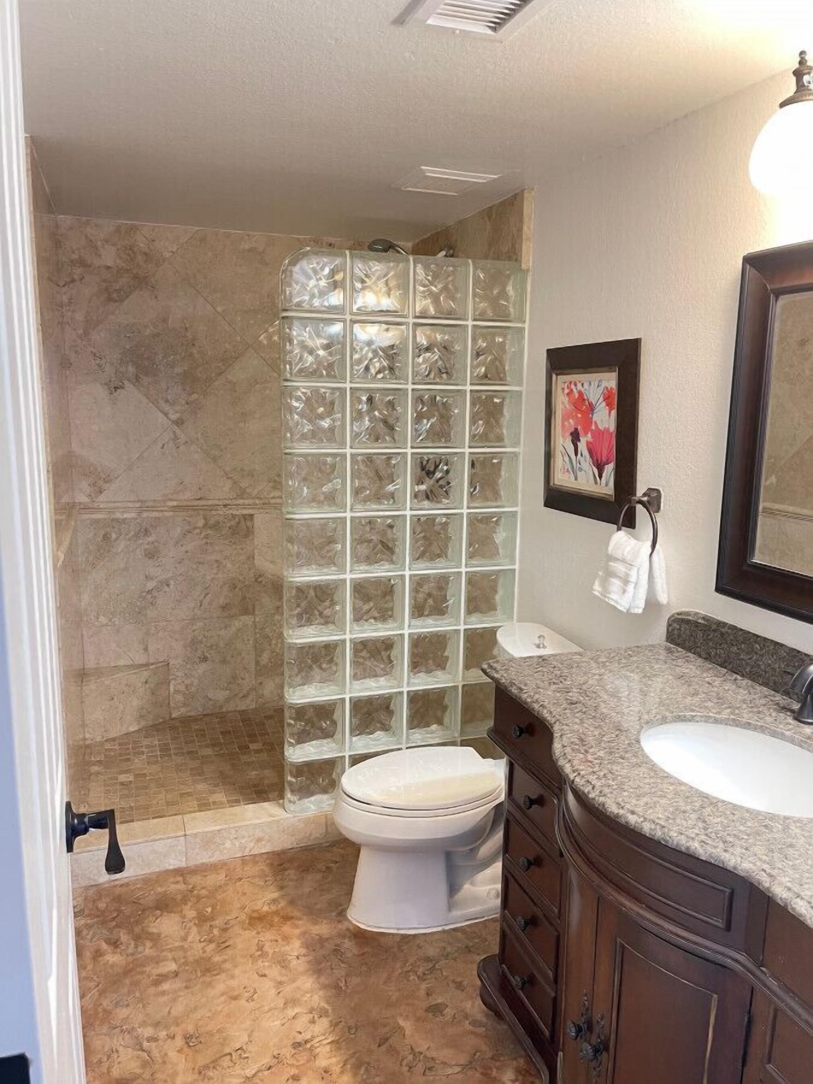 A bathroom with a glass shower enclosure, a toilet, a sink, and a vanity with drawers.