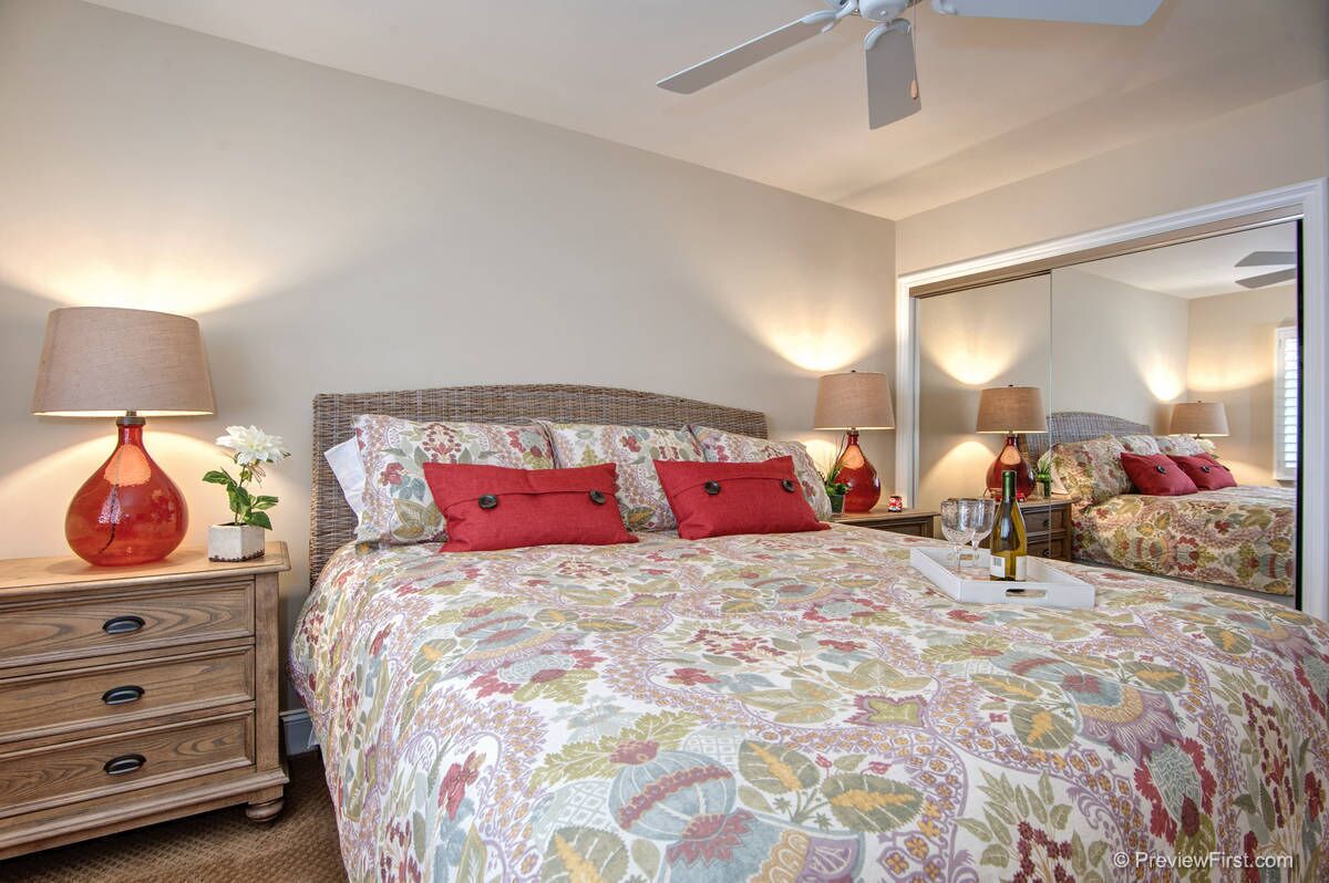 A bedroom with a large bed, two bedside tables, a mirror, and a ceiling fan.