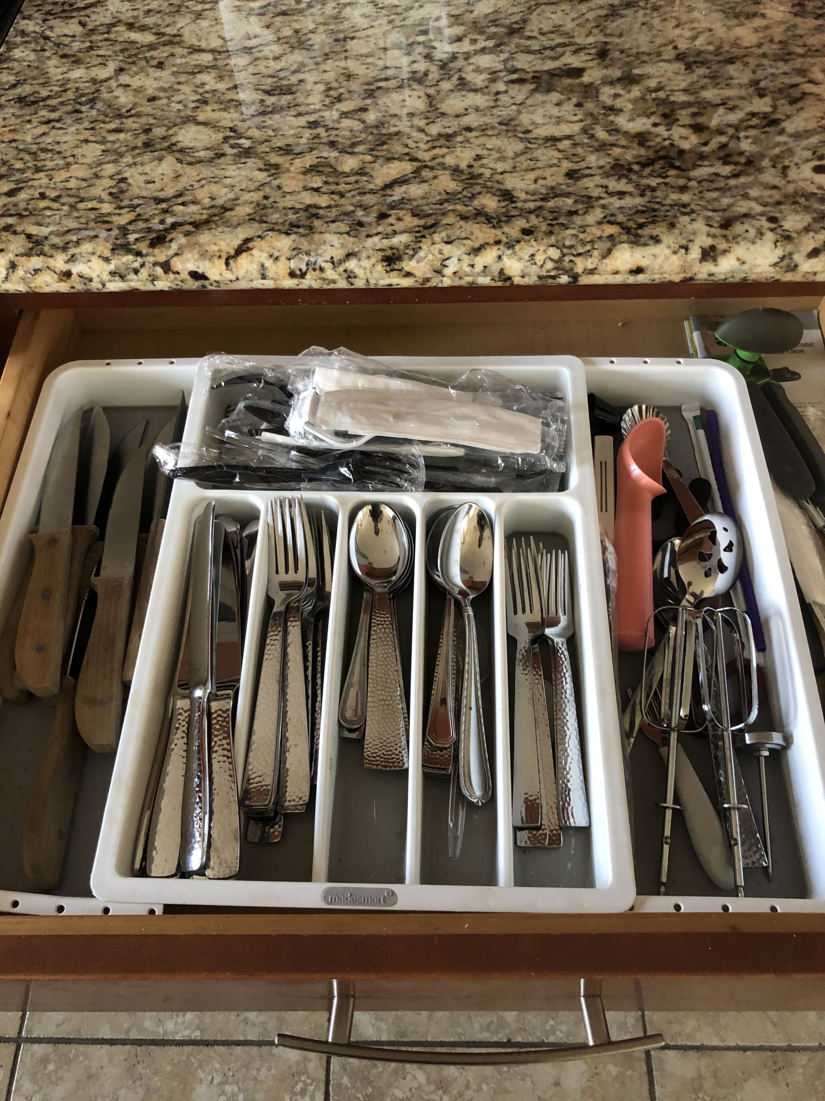 A drawer with utensils and kitchen tools, including knives, forks, spoons, and a grater.