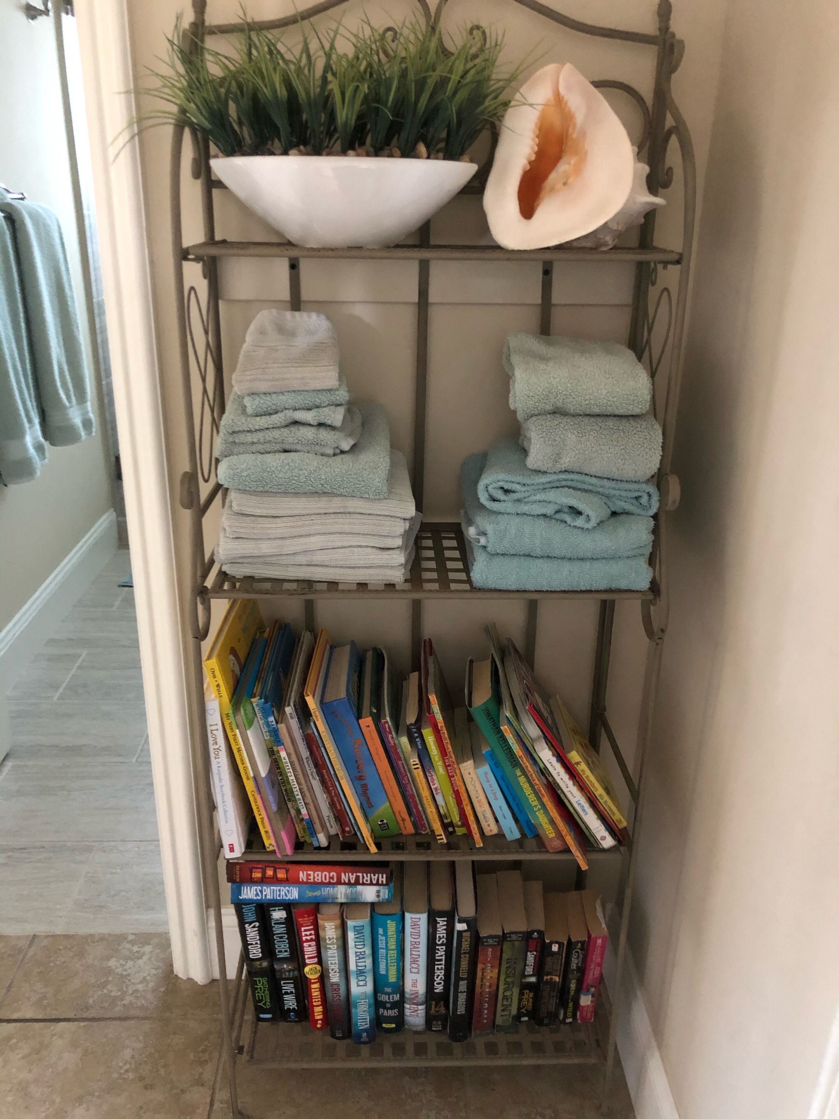 A metal shelf with folded towels, a potted plant, and a seashell.