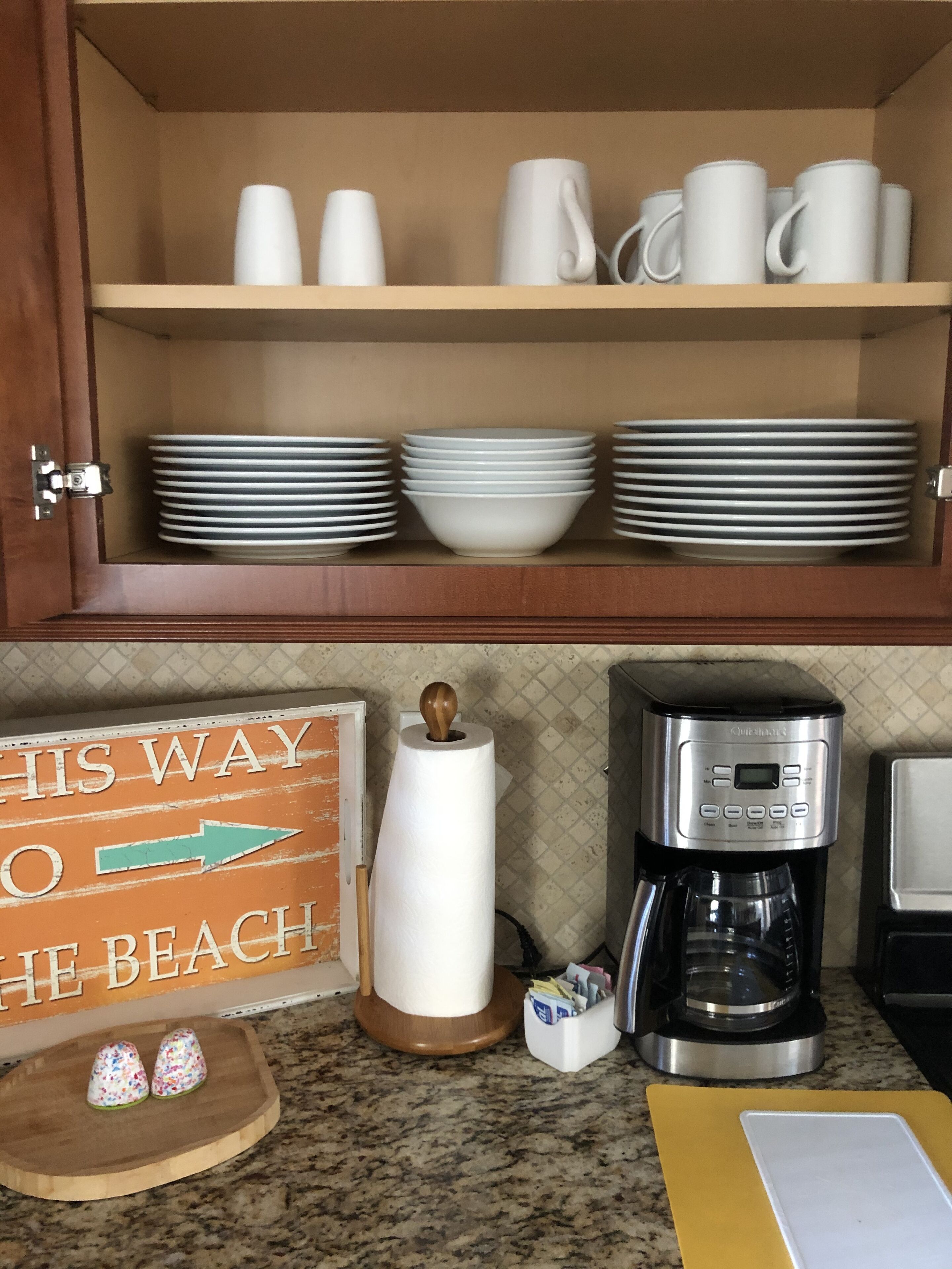 A kitchen with a coffee maker, a sign reading "This Way to the Beach," and a wooden cutting board with decorative items.