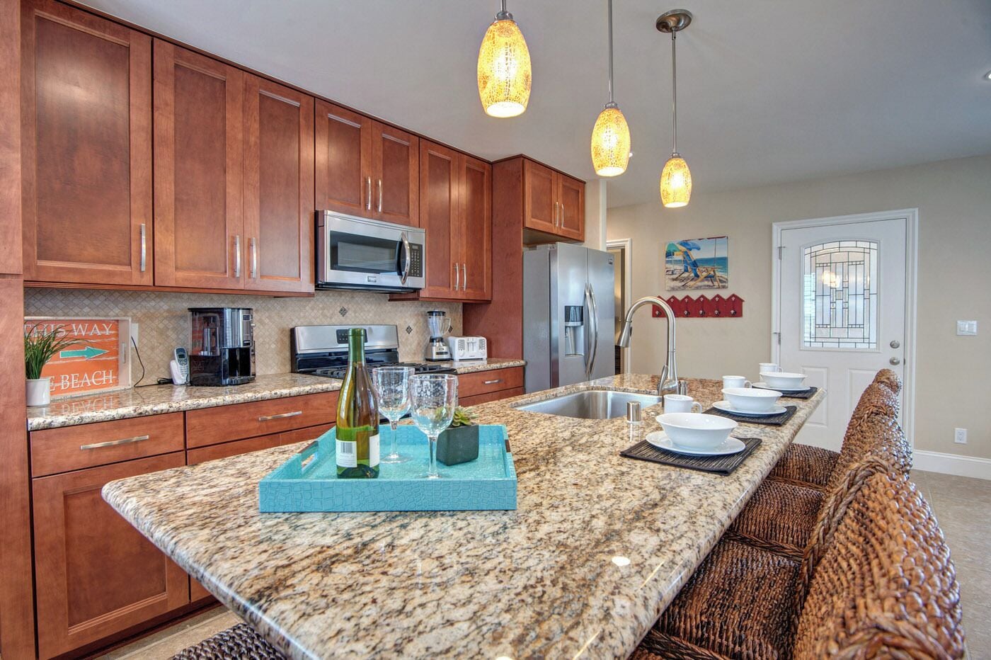 A kitchen with wooden cabinets, granite countertops, a stainless steel refrigerator, a microwave, and pendant lights.