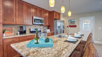 A kitchen with wooden cabinets, granite countertops, a stainless steel refrigerator, a microwave, and pendant lights.