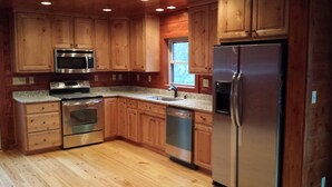 A kitchen with wooden cabinets, stainless steel appliances, a granite countertop, and a window.