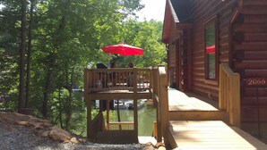 A wooden cabin with a deck overlooking a body of water, a red umbrella, and a sign with the number 2066.