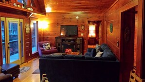 A cozy log cabin interior with a fireplace, a television, and a comfortable seating area.