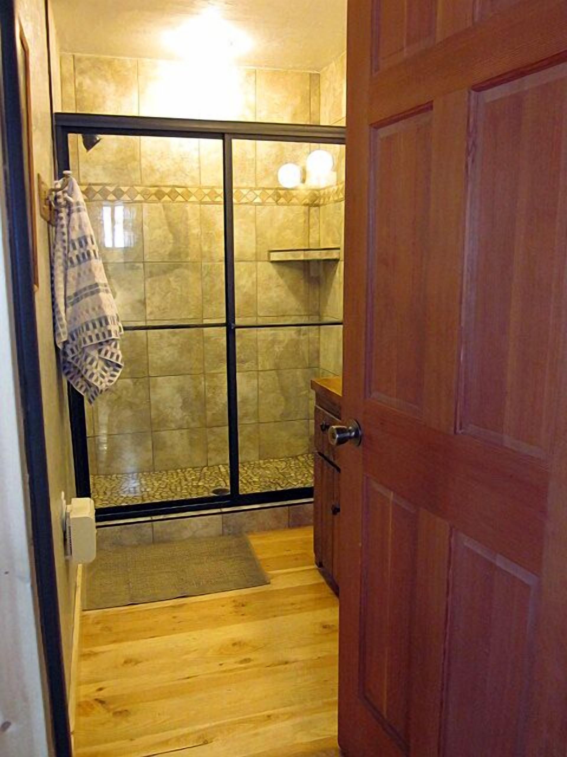 Un bagno con porta doccia in vetro, pavimento in legno, un asciugamano appeso al muro e un armadietto in legno.