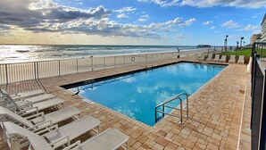 A pool area with a view of the ocean, a deck with lounge chairs, and a building in the background. - Penthouse Suite! Spacious End Corner Unit! 3Bedroom 3 Bath! New Pool 2024 (Daytona Beach)
