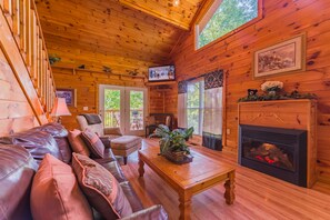 Ein gemütliches Blockhauss-Interieur mit einer Ledersofa, einem Kamin und einem Fernseher.