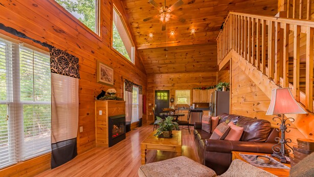 Ein Interieur einer Blockhütte mit einer Holztreppe, einem Wohnzimmer inklusive Sofa und Couchtisch sowie einer Küchenzeile.