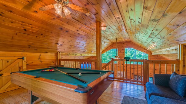 A wooden interior with a pool table, a sofa, and a view of greenery outside. - Gatlinburg/Pigeon Forge Area Secluded, Luxury Cabin, Hot Tub,Fireplace, King Bed (Sevierville)