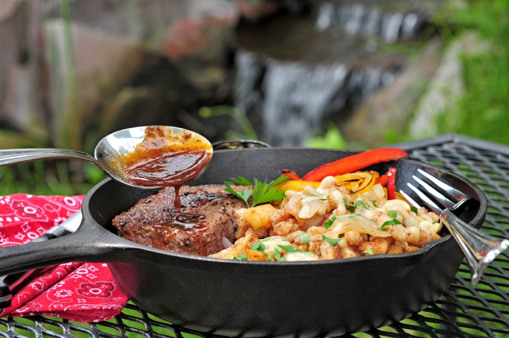 A meal served in a skillet on a metal table with a red napkin and utensils.