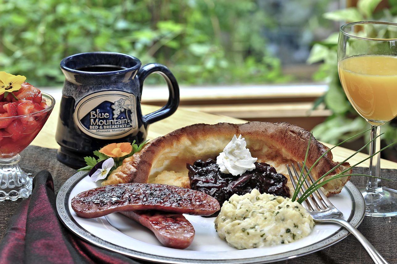 A breakfast plate with sausage, mashed potatoes, and a muffin, accompanied by a mug and a glass of orange juice.