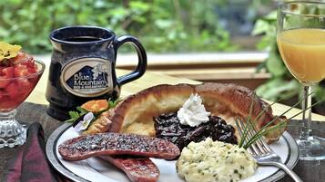 A breakfast plate with sausage, mashed potatoes, and a muffin, accompanied by a mug and a glass of orange juice.