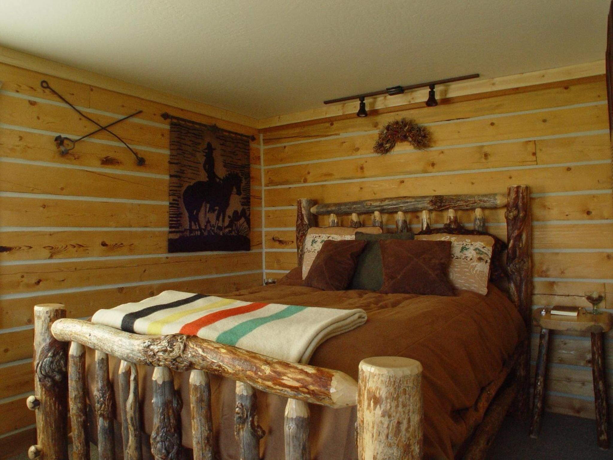 A rustic wooden room with a bed, a wall-mounted light fixture, and a horse silhouette artwork.