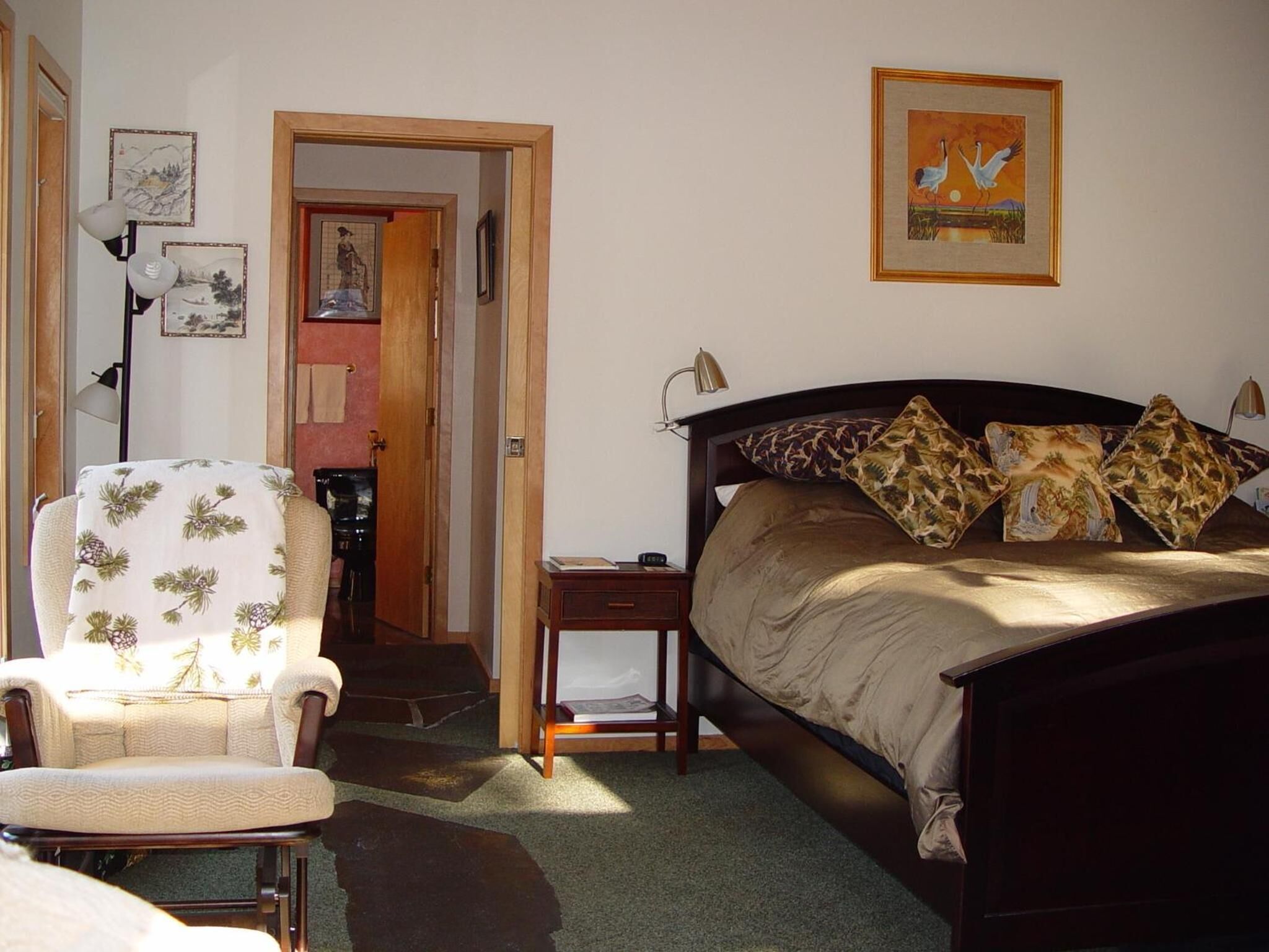 A bedroom with a bed, a chair, a nightstand, and a door leading to another room.