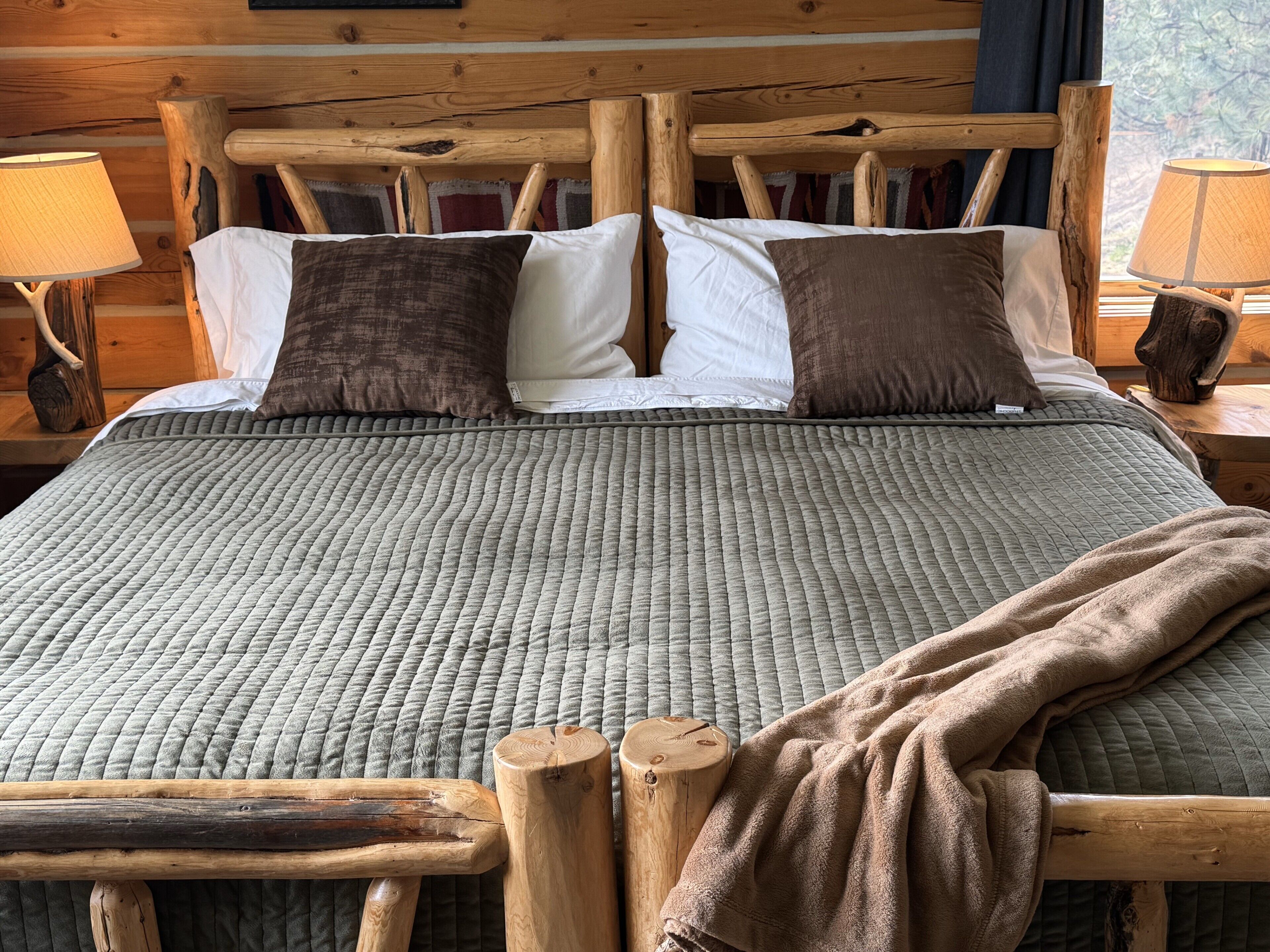 A bed with a grey quilted bedspread, wooden headboard, and two nightstands with lamps.