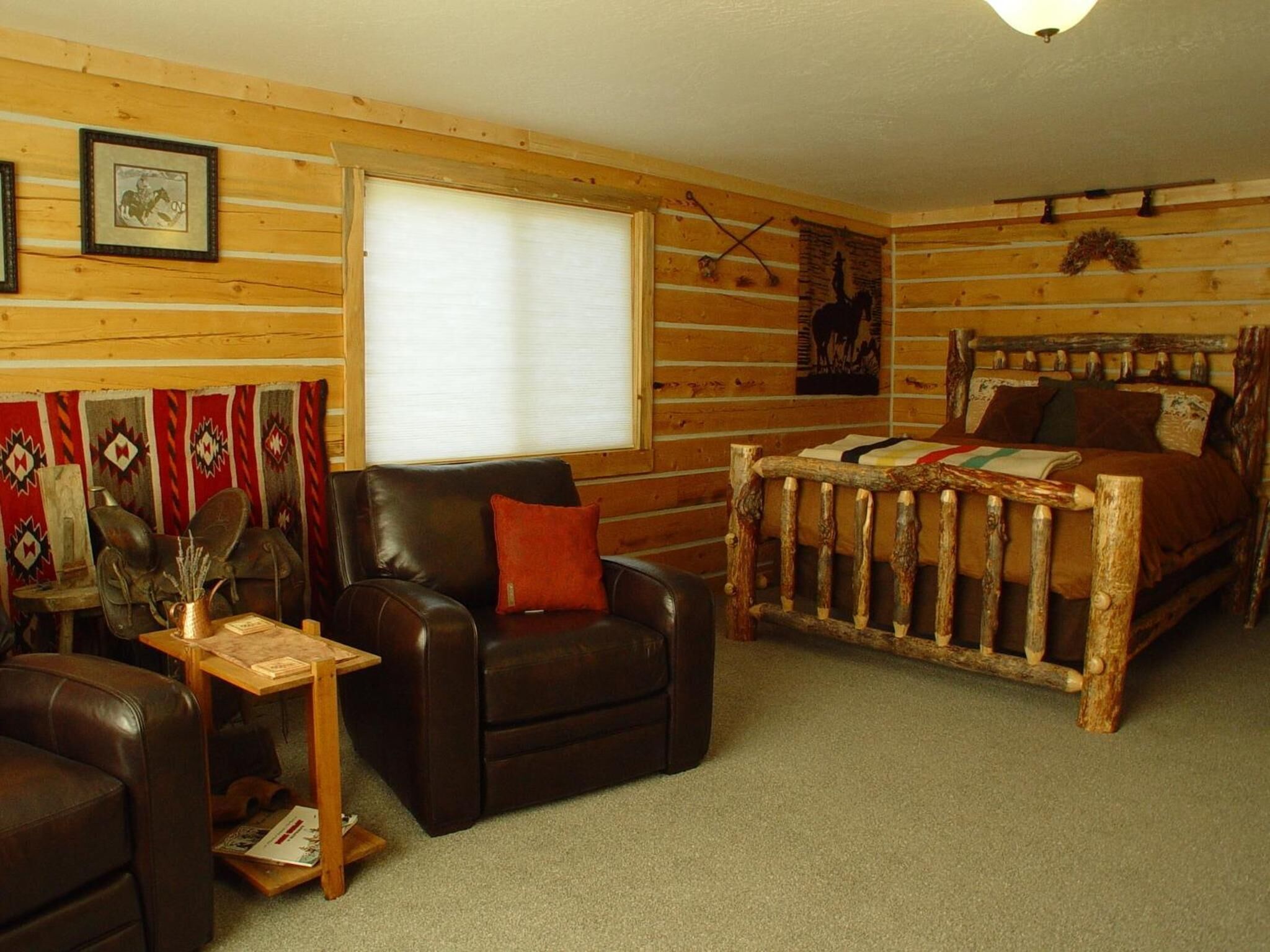 A log cabin room with a leather sofa, a wooden bed, and a window with blinds.