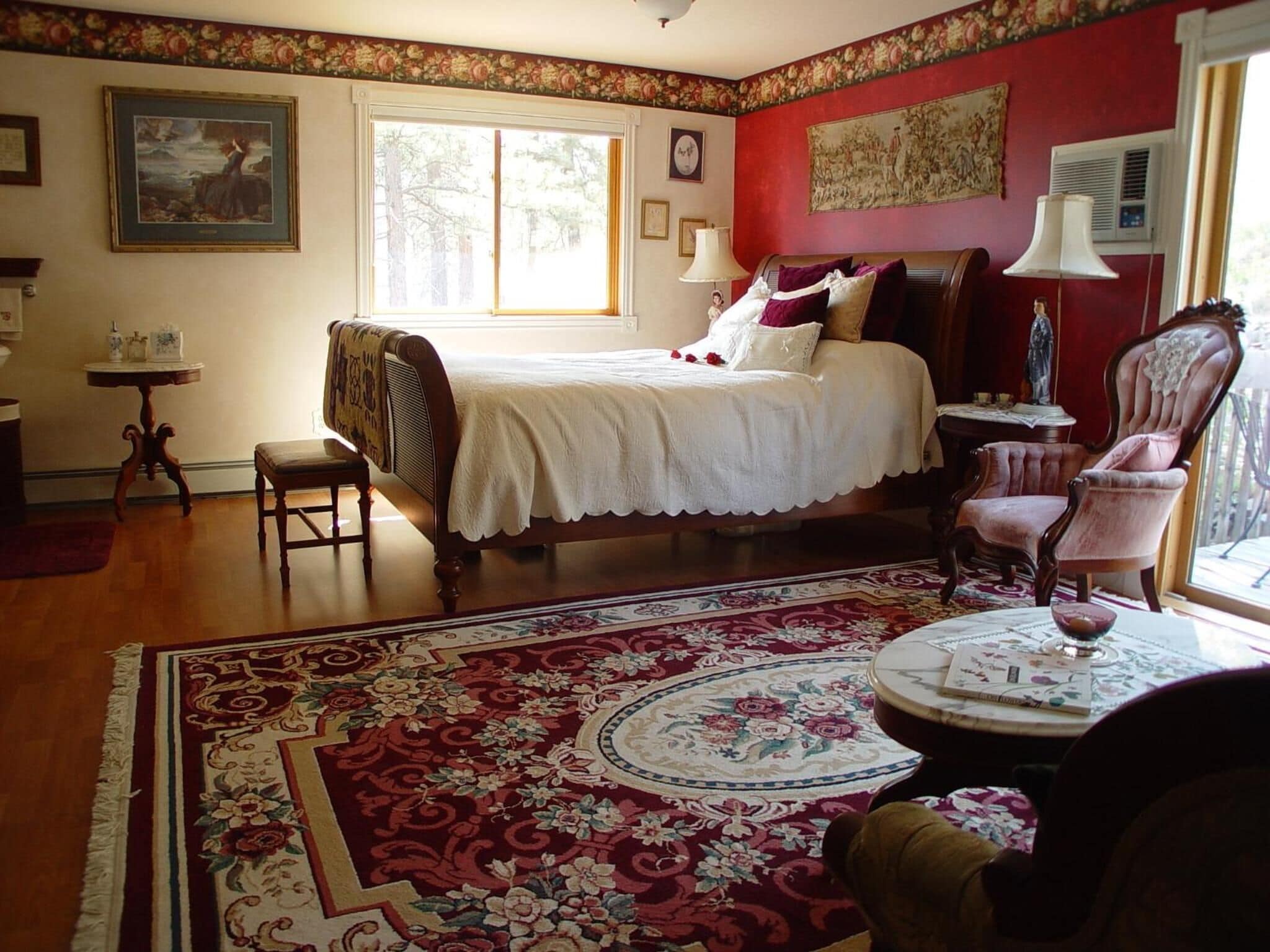 A traditional bedroom with a large bed, a chair, a small table, and a window.