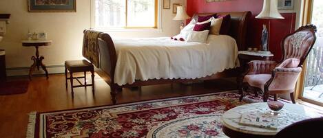A traditional bedroom with a large bed, a chair, a small table, and a window.