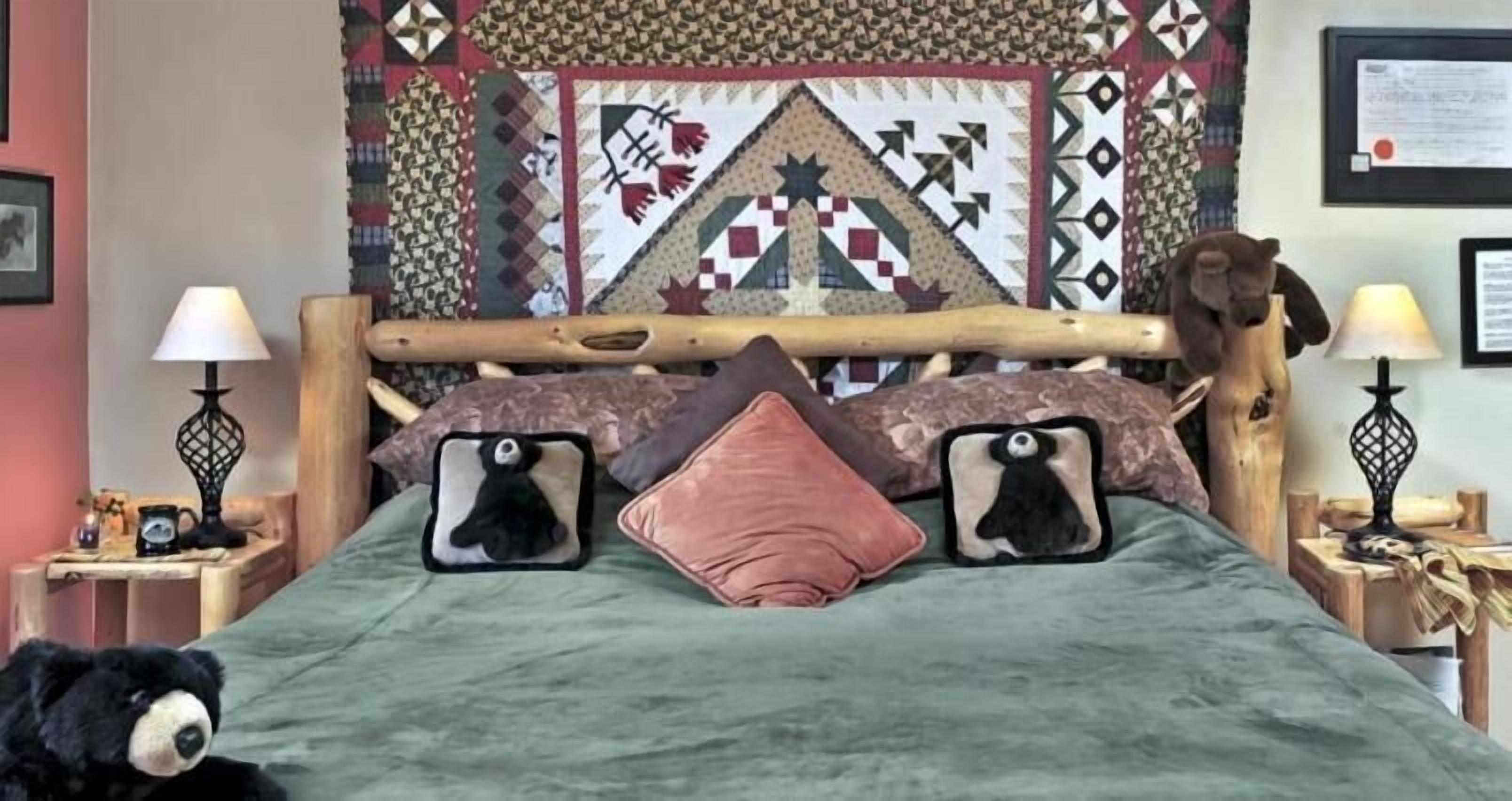 A bed with a green blanket, two pillows with bear designs, a wooden headboard, and a quilt with geometric patterns.