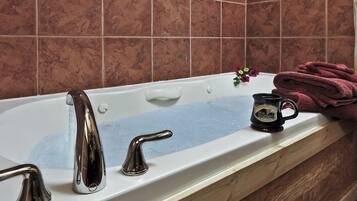 A bathroom with a bathtub, two faucets, a flower vase, and a rolled-up towel.