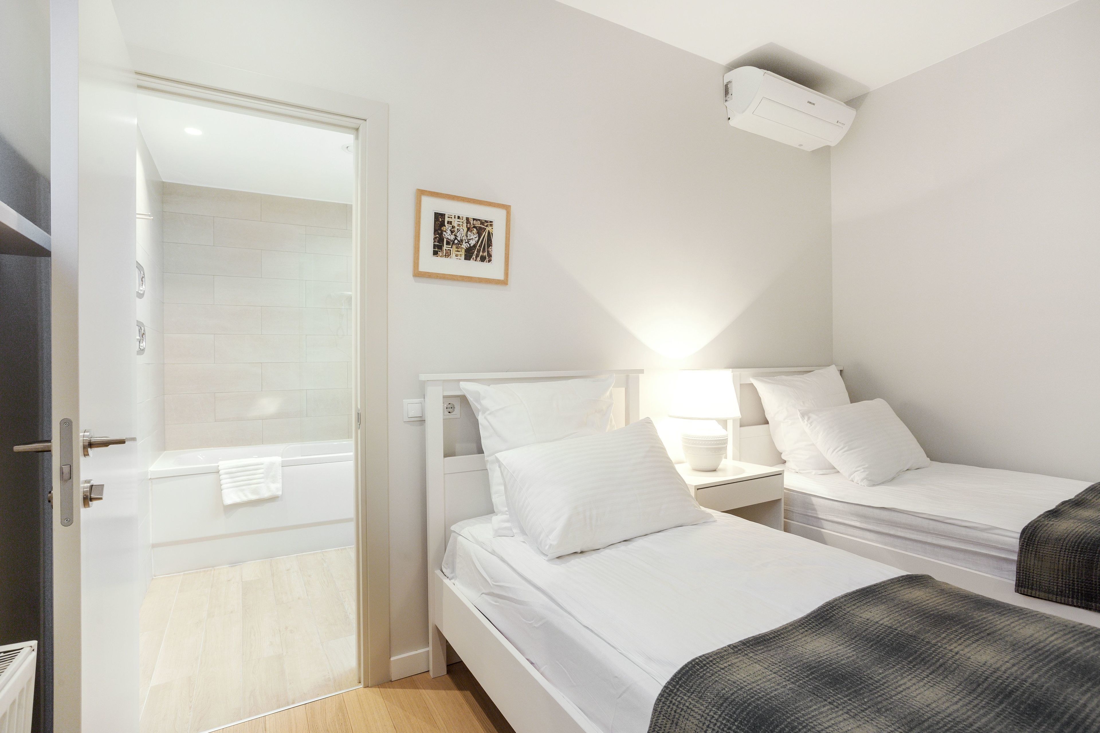 A modern bedroom with two beds, a shower, and a small bedside table with a lamp.