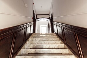 Una scala in marmo con ringhiere in legno conduce a una stanza luminosa.