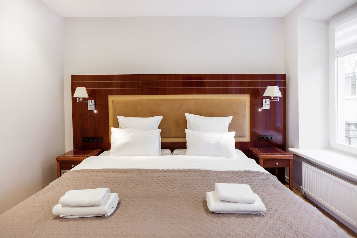 Una habitación de hotel con una cama grande, dos mesitas de noche y una ventana con vistas.