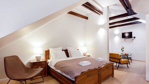 A modern bedroom with a sloped ceiling, a wooden bed, a nightstand, a chair, and a TV mounted on the wall. - Jolly apartments (Vilnius)