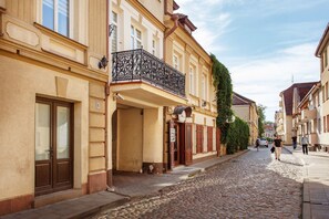 A cobblestone street lined with historic buildings, featuring balconies with wrought iron railings and a mix of architectural styles. - Jolly apartments (Vilnius)