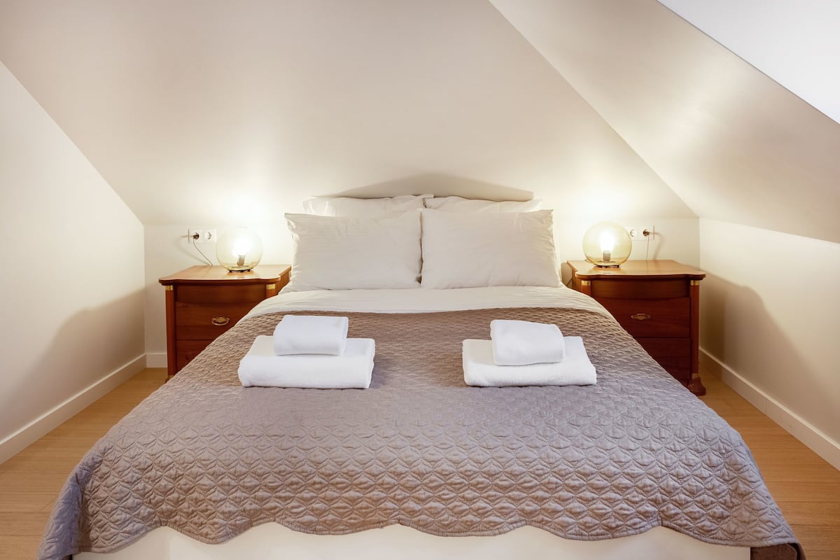 Una cama bien hecha con un cubrecolcha acolchado, dos mesitas de noche con lámparas y un cabecero de madera.