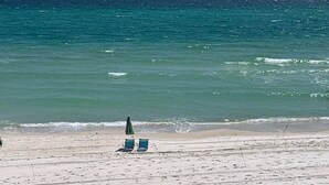 Una spiaggia con due sdraio blu e un ombrellone verde sotto un cielo sereno.