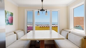 A dining area with a table and benches, large windows with a view of the beach, and a ceiling light fixture. - BEACH FRONT LUXURY VENETIAN - 2 Jacuzzi Tubs - 2 Parking Passes - BBQ (Capitola)