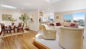 A spacious living area with a dining table, chairs, and a sofa set. There is a kitchen in the background with a view of the sea. - BEACH FRONT LUXURY VENETIAN - 2 Jacuzzi Tubs - 2 Parking Passes - BBQ (Capitola)